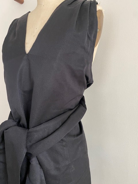 A pre-owned Dries Van Noten heavy silk faille wrap dress displayed on a mannequin, featuring a deep V-neck neckline, large bow tie at the waist, and tuck shoulder detail.